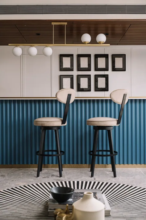 A Mumbai apartment counter corner with blue fluted cabinetry, brass trim, high chairs and framed photographs