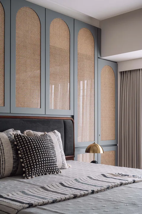 A Mumbai apartment bedroom with arched cane-front storage behind the bed, timber panelling and grey bedding